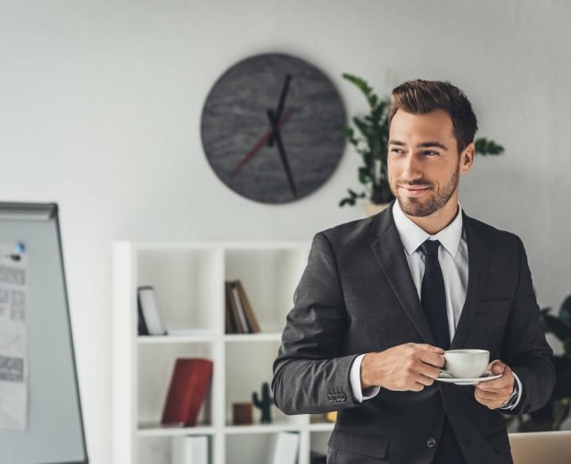 happy-young-businessman-with-cup-of-coffee-at-offi-2021-08-31-22-17-08-utc.jpg